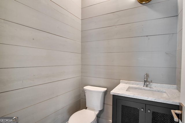 bathroom featuring wooden walls, vanity, and toilet