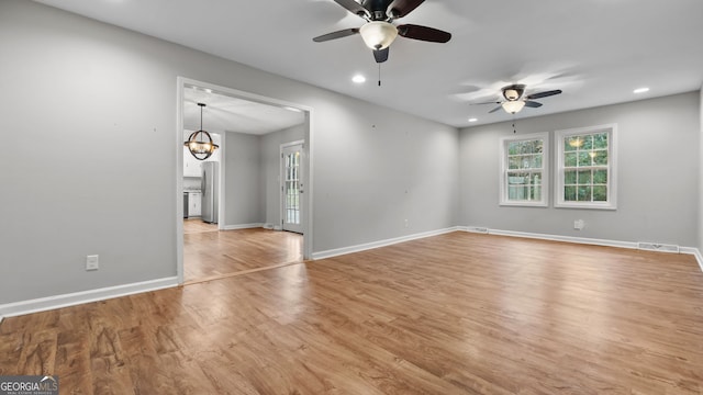 unfurnished room with ceiling fan with notable chandelier and light hardwood / wood-style flooring