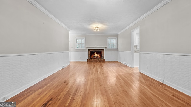 unfurnished living room featuring light hardwood / wood-style floors, ornamental molding, and a brick fireplace