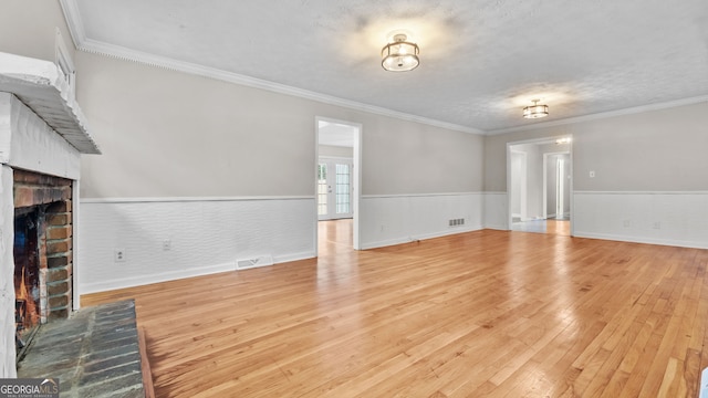 unfurnished living room with a brick fireplace, crown molding, a textured ceiling, and light hardwood / wood-style flooring