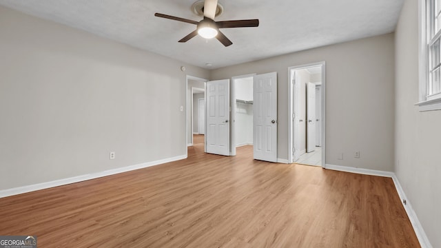 unfurnished bedroom with a spacious closet, a closet, light wood-type flooring, ceiling fan, and ensuite bathroom