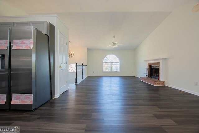 unfurnished living room featuring dark hardwood / wood-style flooring, ceiling fan with notable chandelier, a brick fireplace, and vaulted ceiling