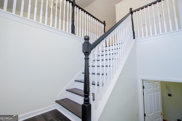 stairway with hardwood / wood-style floors and a towering ceiling