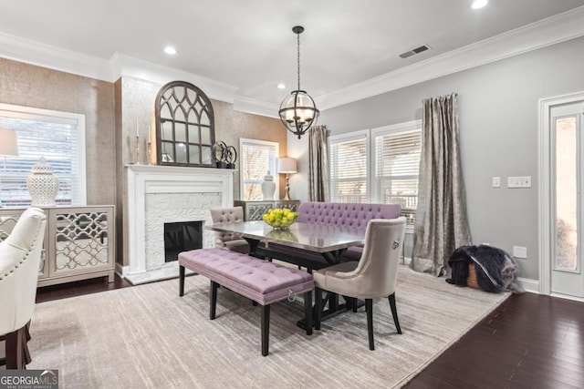 dining room featuring hardwood / wood-style flooring, a stone fireplace, ornamental molding, and a chandelier