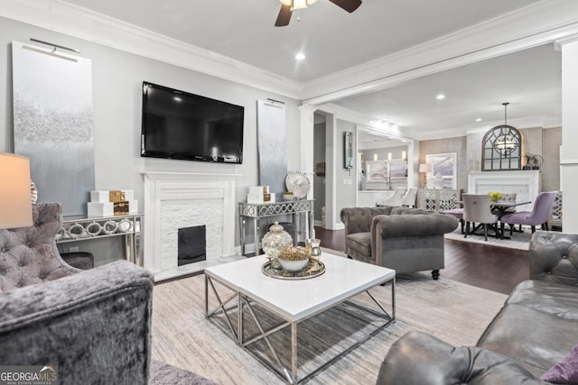 living room featuring hardwood / wood-style flooring, a stone fireplace, ceiling fan, and crown molding