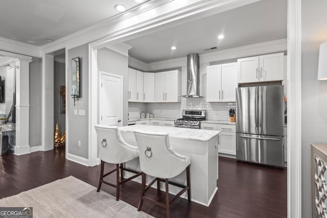 kitchen with a breakfast bar, a center island, wall chimney range hood, white cabinetry, and stainless steel appliances