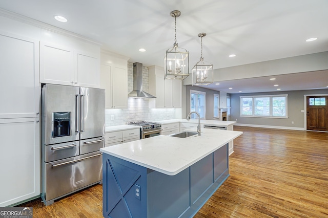 kitchen featuring wall chimney exhaust hood, white cabinets, a sink, premium appliances, and backsplash