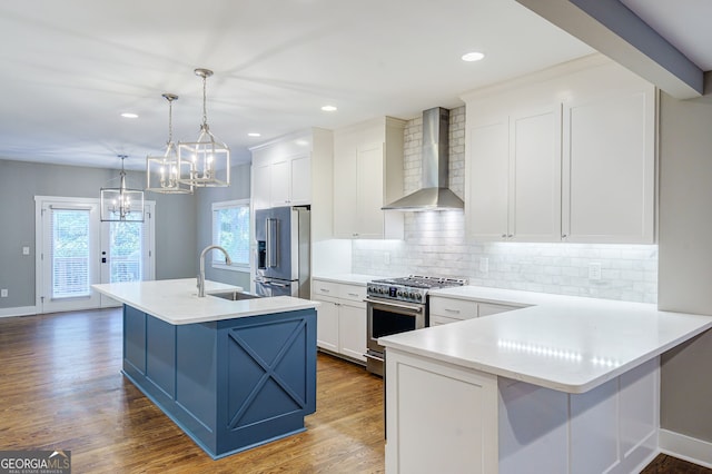 kitchen featuring pendant lighting, a center island with sink, wall chimney range hood, premium appliances, and white cabinetry