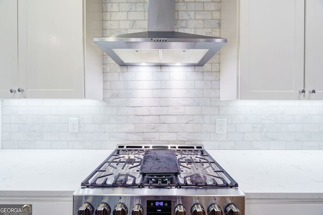 kitchen featuring wall chimney range hood, white cabinetry, light stone counters, gas stove, and decorative backsplash