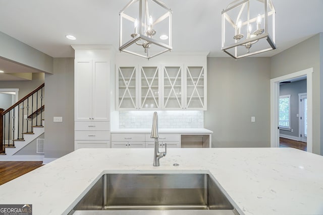 kitchen with a chandelier, tasteful backsplash, light stone counters, and sink