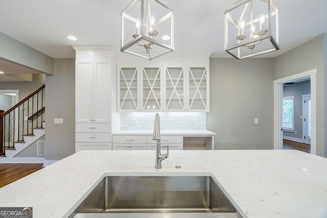 kitchen with a notable chandelier, a sink, wood finished floors, decorative backsplash, and light stone counters