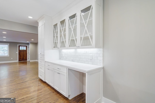 interior space with tasteful backsplash, baseboards, glass insert cabinets, white cabinets, and wood finished floors