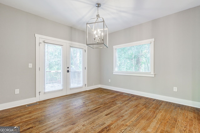 unfurnished dining area with a chandelier, wood finished floors, french doors, and visible vents