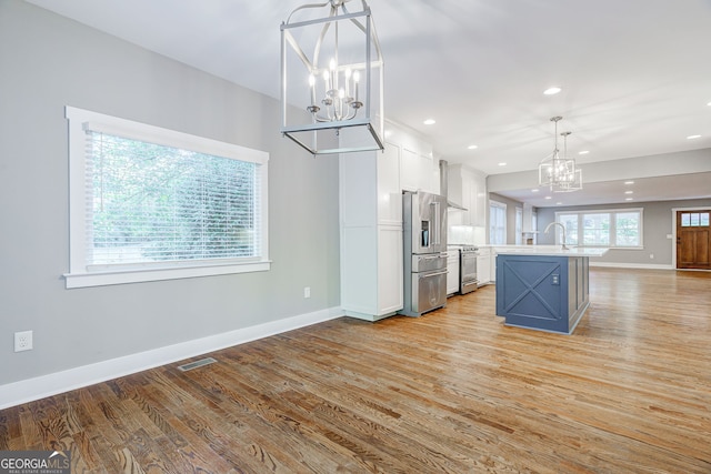 kitchen with hanging light fixtures, a chandelier, a center island with sink, white cabinets, and appliances with stainless steel finishes