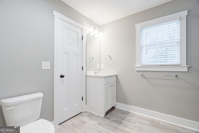 bathroom with toilet, wood finished floors, vanity, and baseboards