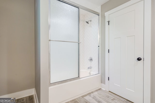 bathroom with baseboards, wood finished floors, and bath / shower combo with glass door