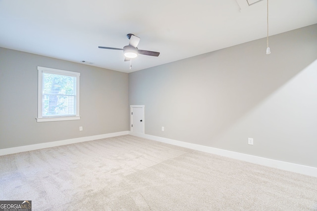 carpeted empty room featuring visible vents, baseboards, attic access, and a ceiling fan