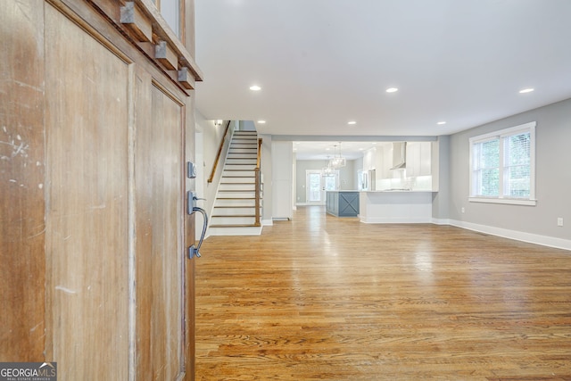unfurnished living room featuring recessed lighting, light wood-style flooring, stairway, and baseboards