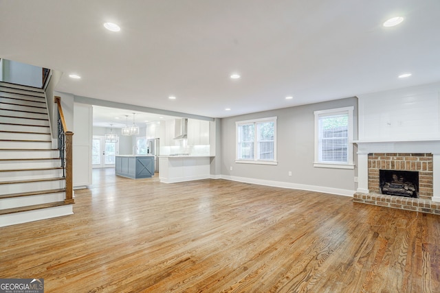 unfurnished living room featuring light wood-type flooring, recessed lighting, a brick fireplace, stairs, and baseboards