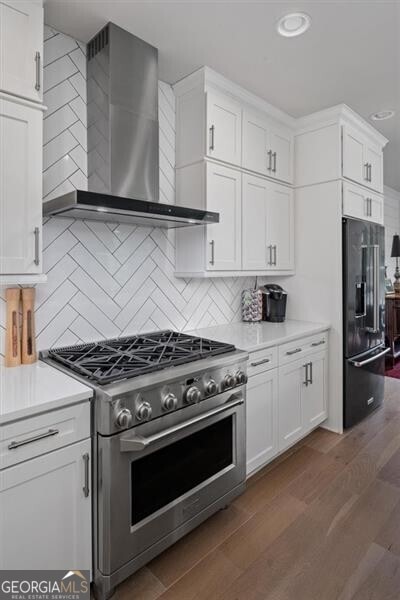 kitchen featuring high quality appliances, white cabinets, wall chimney range hood, and tasteful backsplash