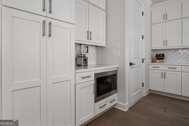 bar with backsplash, white cabinets, black microwave, and dark hardwood / wood-style flooring