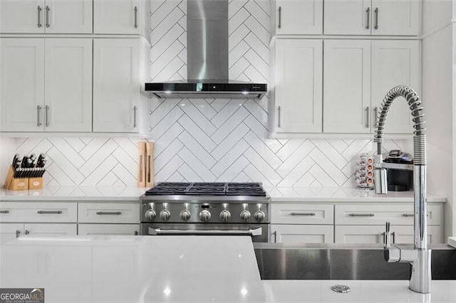 kitchen with wall chimney range hood, tasteful backsplash, white cabinetry, and high end stainless steel range