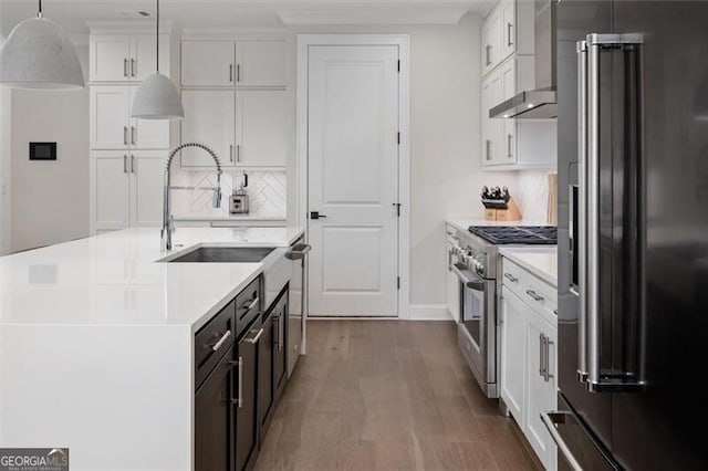 kitchen with hanging light fixtures, premium appliances, a kitchen island with sink, white cabinetry, and sink