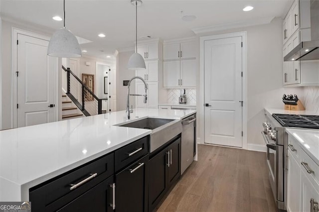 kitchen featuring decorative light fixtures, white cabinets, appliances with stainless steel finishes, and wall chimney range hood