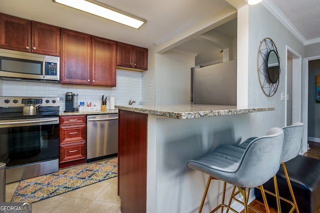 kitchen featuring kitchen peninsula, light tile patterned floors, stainless steel appliances, and a breakfast bar area