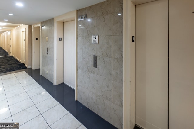 corridor featuring dark tile patterned floors, tile walls, and elevator