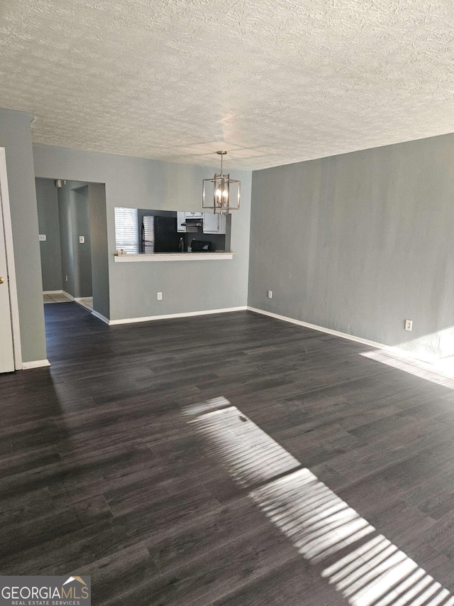 unfurnished living room with a chandelier, a textured ceiling, and dark wood-type flooring