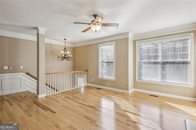 empty room featuring ceiling fan with notable chandelier, light hardwood / wood-style floors, decorative columns, and crown molding