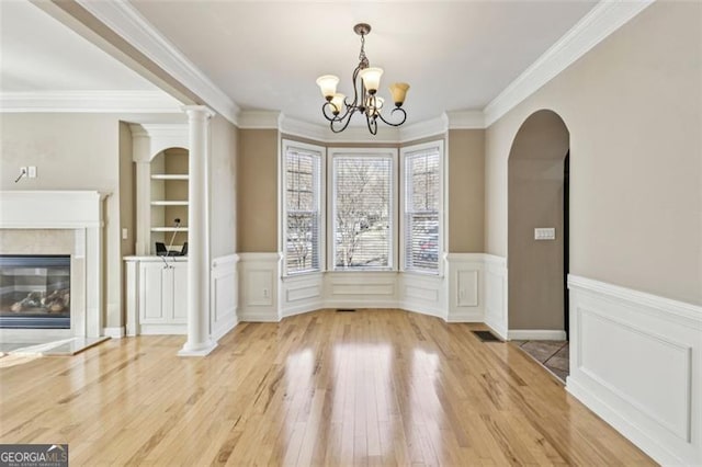 unfurnished dining area featuring crown molding, built in features, hardwood / wood-style floors, and an inviting chandelier