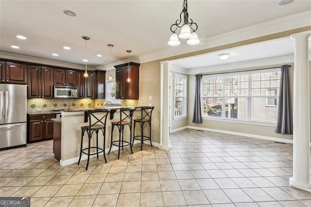 kitchen with decorative backsplash, appliances with stainless steel finishes, decorative light fixtures, a breakfast bar area, and decorative columns