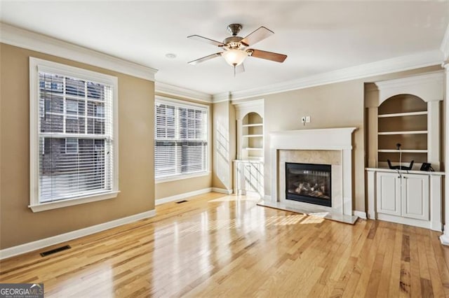 unfurnished living room with built in shelves, wood-type flooring, ornamental molding, and a high end fireplace