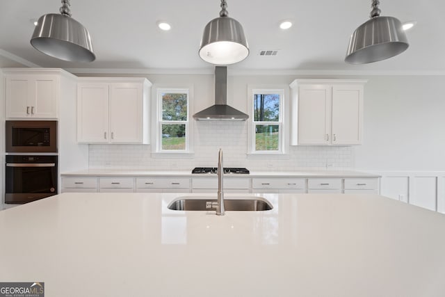 kitchen featuring white cabinets, appliances with stainless steel finishes, decorative light fixtures, and wall chimney range hood