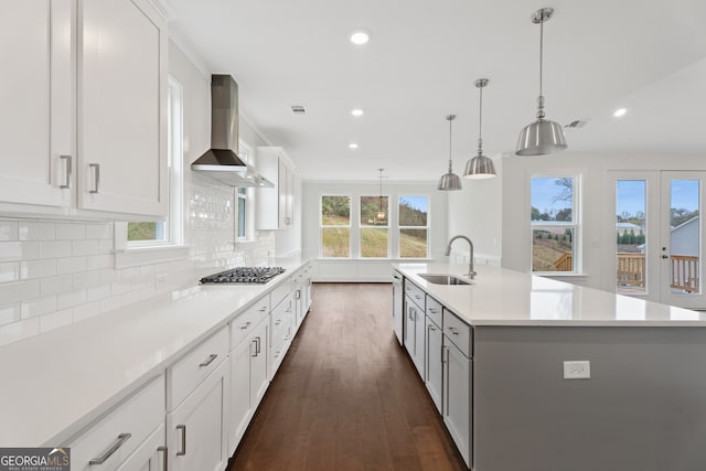 kitchen featuring wall chimney range hood, sink, hanging light fixtures, a large island, and white cabinetry