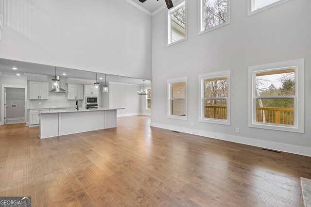 kitchen featuring white cabinetry, hanging light fixtures, stainless steel appliances, wall chimney range hood, and decorative backsplash