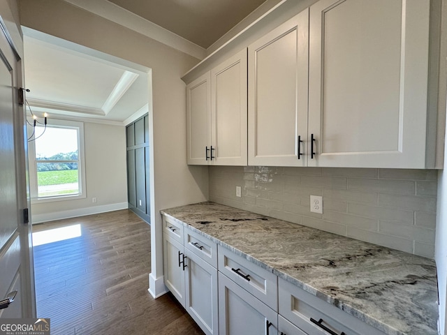 kitchen featuring crown molding, light stone countertops, tasteful backsplash, white cabinetry, and wood-type flooring