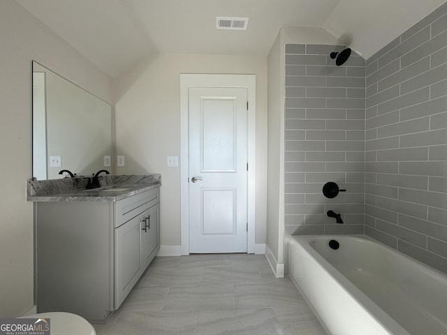 bathroom with vanity, tiled shower / bath, and vaulted ceiling