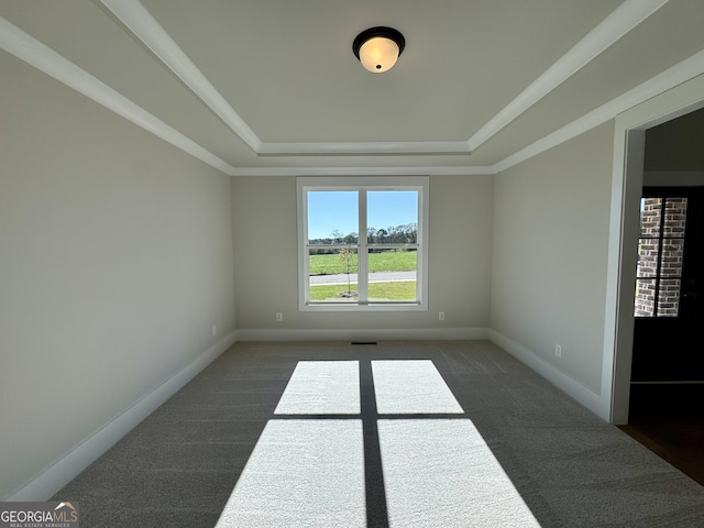 empty room with dark colored carpet, a raised ceiling, and crown molding