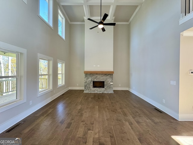 unfurnished living room featuring coffered ceiling, a stone fireplace, dark hardwood / wood-style floors, ceiling fan, and beamed ceiling