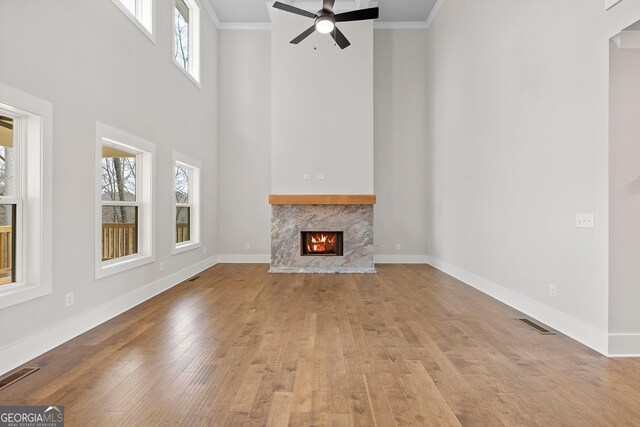 unfurnished living room featuring a high end fireplace, a high ceiling, ceiling fan with notable chandelier, and a wealth of natural light