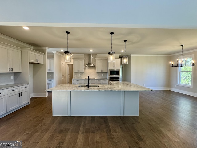 kitchen featuring sink, an island with sink, pendant lighting, and wall chimney range hood