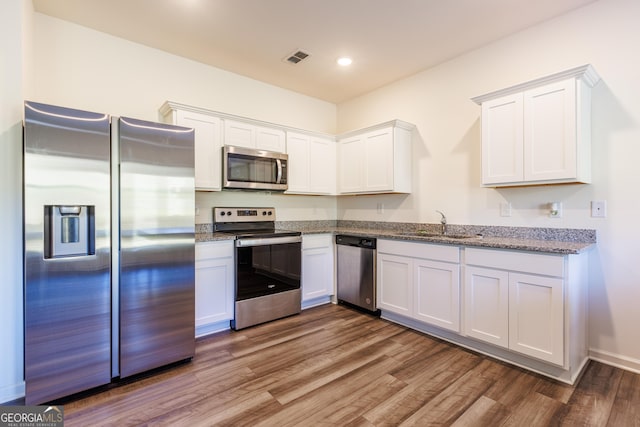 kitchen featuring light stone countertops, sink, dark hardwood / wood-style floors, white cabinets, and appliances with stainless steel finishes