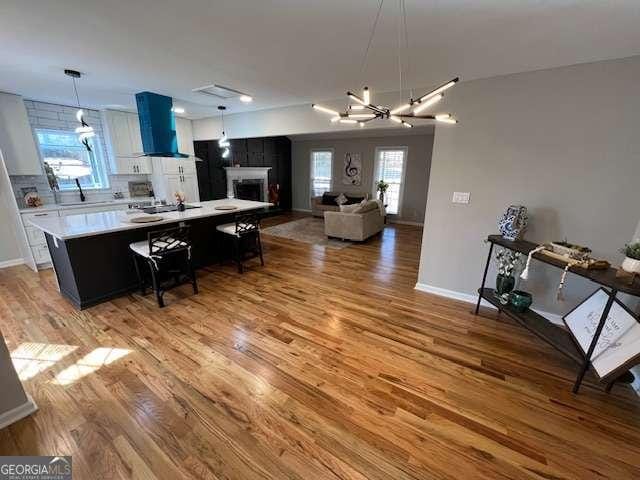 kitchen featuring a kitchen bar, wall chimney exhaust hood, hardwood / wood-style flooring, a notable chandelier, and a kitchen island