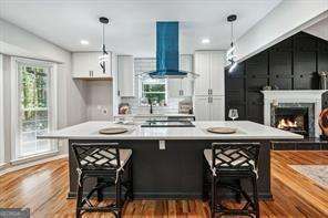 kitchen with white cabinets, hanging light fixtures, range hood, cooktop, and a breakfast bar area