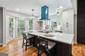 kitchen featuring a kitchen bar, exhaust hood, white cabinets, a center island, and hanging light fixtures