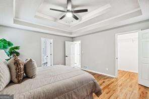 bedroom with wood-type flooring, a raised ceiling, ceiling fan, and crown molding