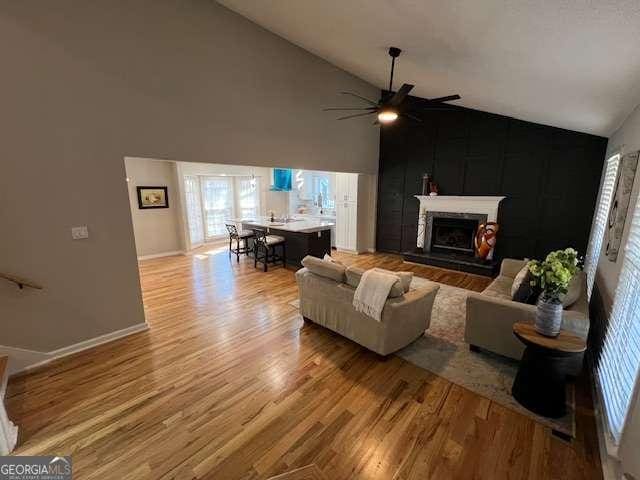 living room with ceiling fan, light hardwood / wood-style flooring, and high vaulted ceiling